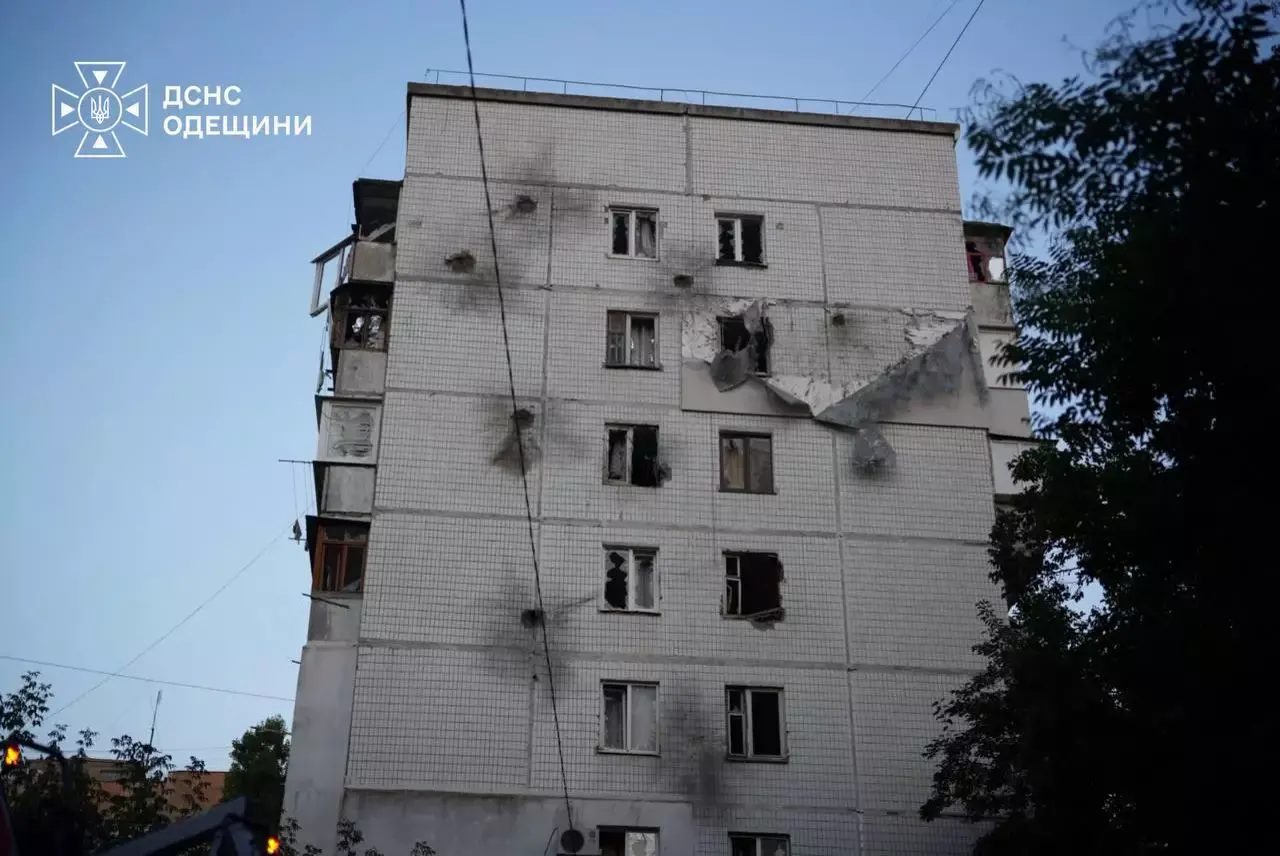 Fachada de un bloque de viviendas de nueve plantas en Odesa al amanecer, picada por impactos de metralla, con ventanas reventadas, balcones calcinados y un trozo de revestimiento arrancado.