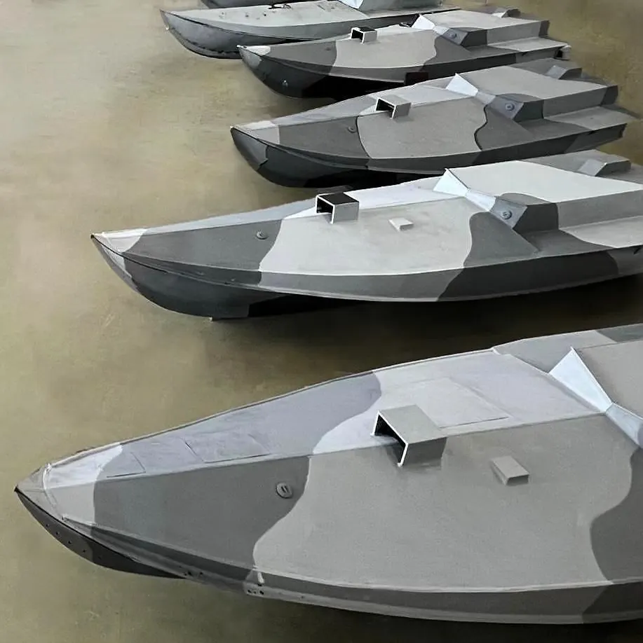 Fila de embarcaciones no tripuladas ucranianas con casco afilado y camuflaje gris, alineadas en el suelo de una nave industrial